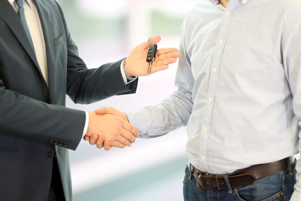 Car salesman handing over the keys for a new car to a young man